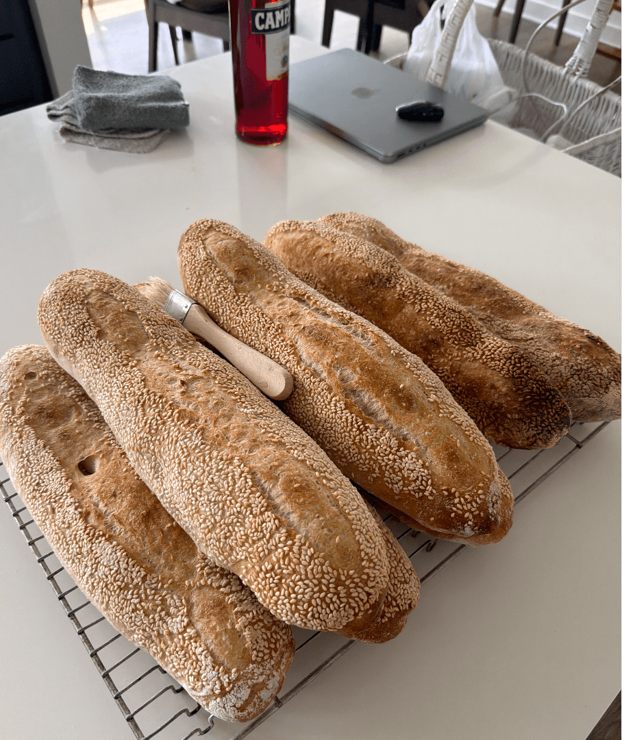 Sesame-crusted sourdough sub rolls cooling on a wire rack